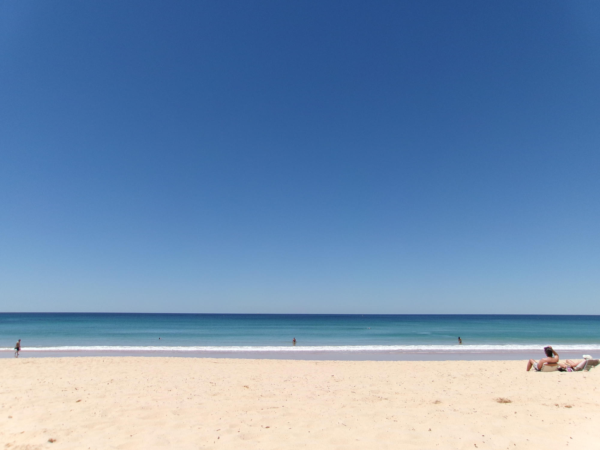 A bright summer beach beneath a wide blue sky.