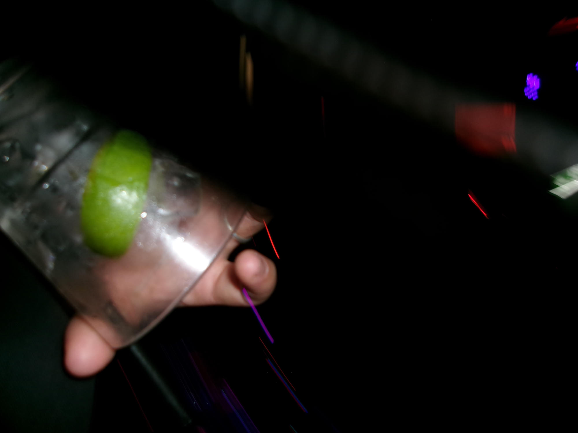 A hand holding a drink with a lime in a dark, colorful setting.