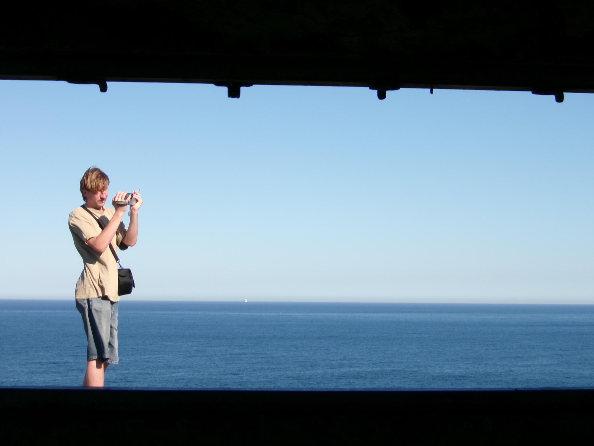 A person holding a camera beside the ocean.