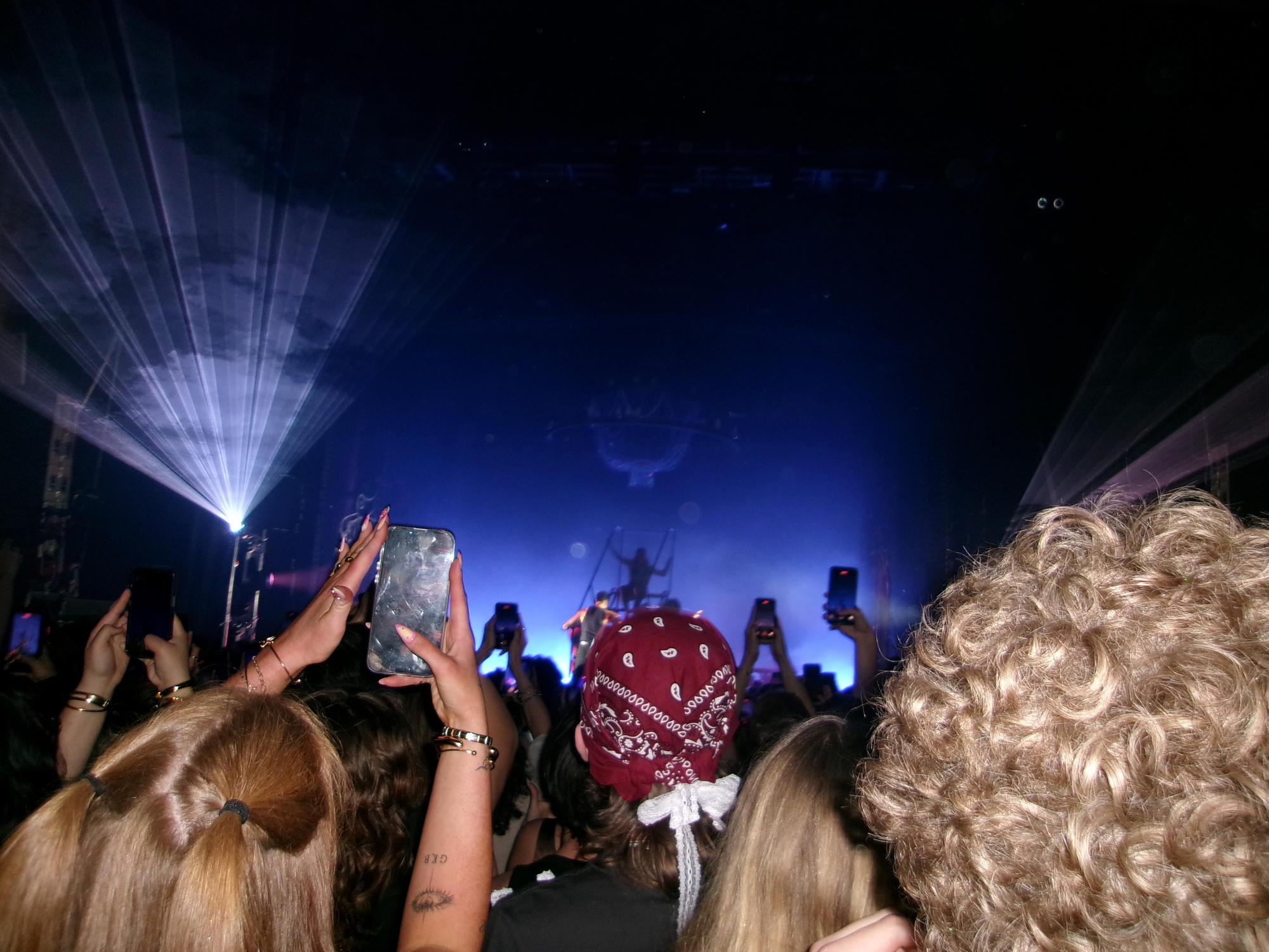 A concert crowd watching a stage lit in blue and purple.
